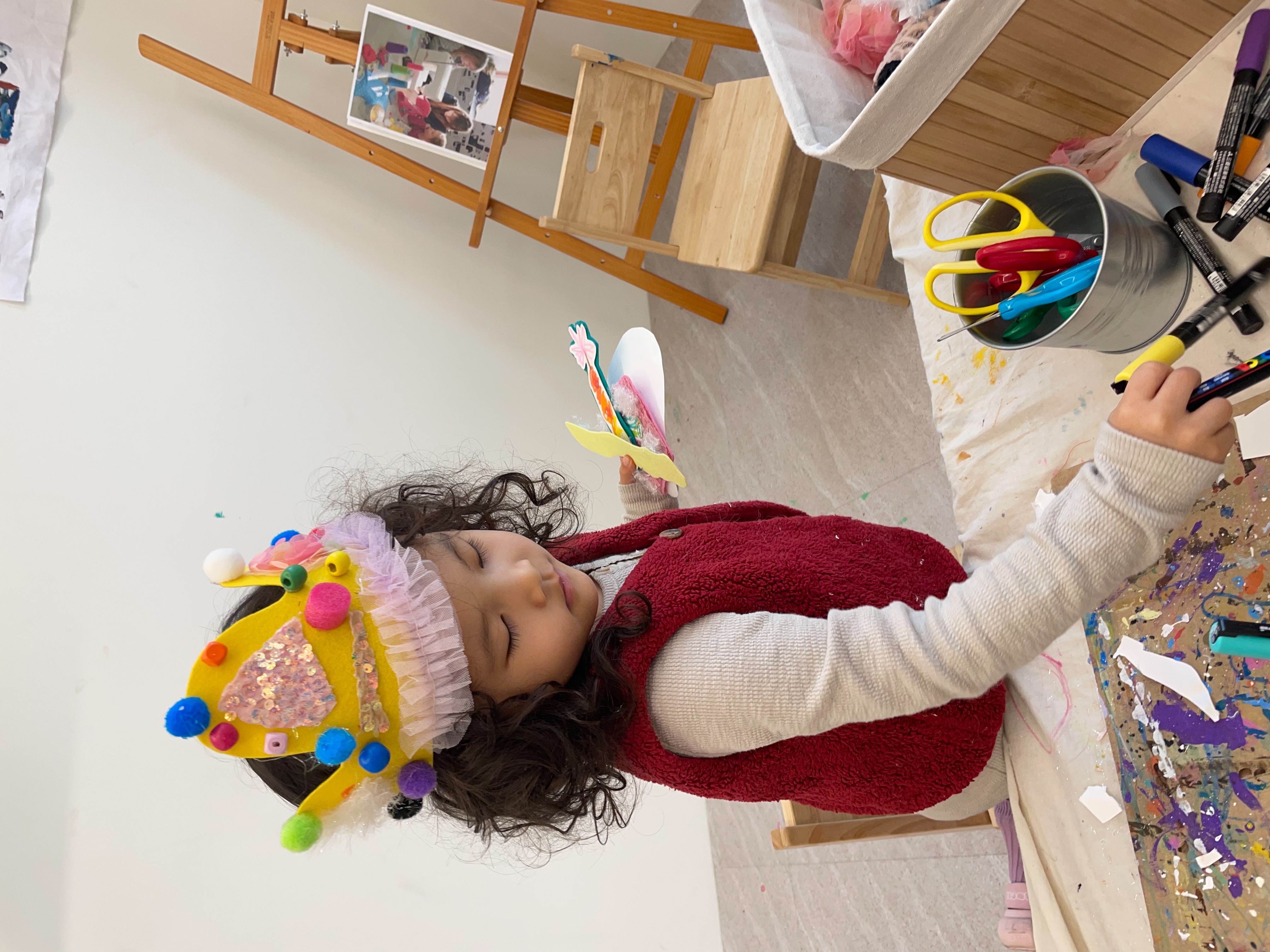 Wearing her handmade crown decorated with colorful pom-poms